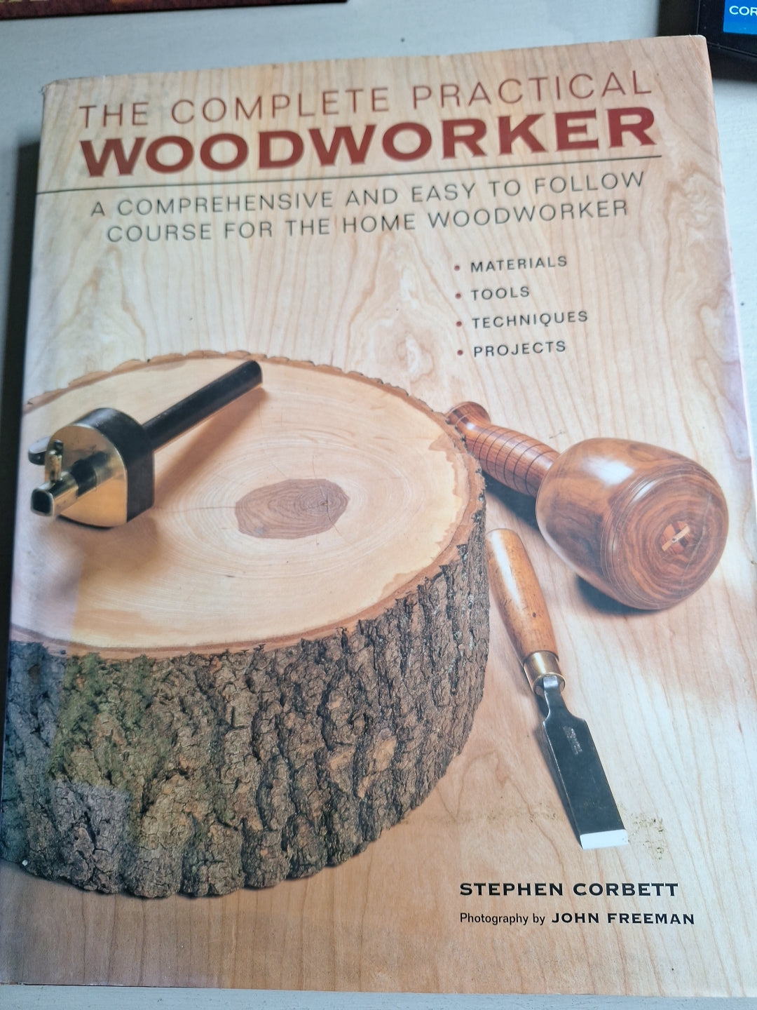 The Complete Practical Woodworker book by Stephen Corbett with woodworking tools on a wood log
