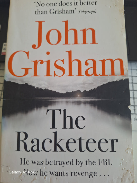 Used John Grisham The Racketeer book featuring a lake and mountain cover design